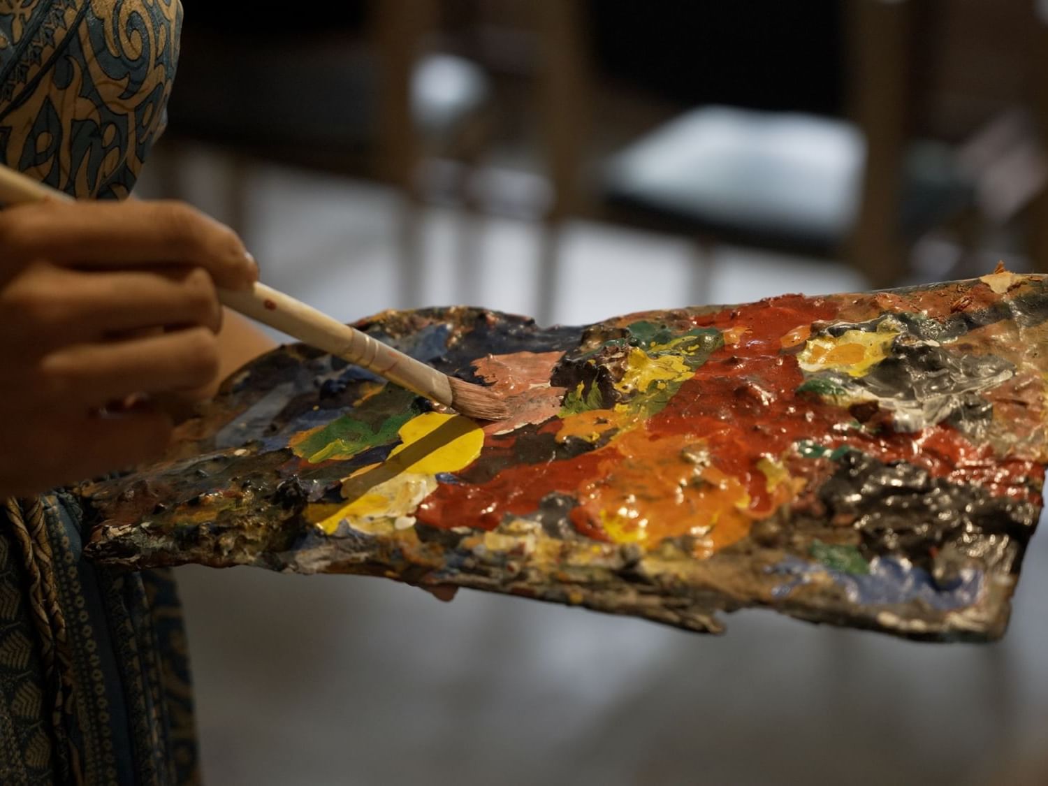 Close-up of a hand holding a paintbrush over a colorful artist's palette at Dwarika's Himalayan Wellbeing