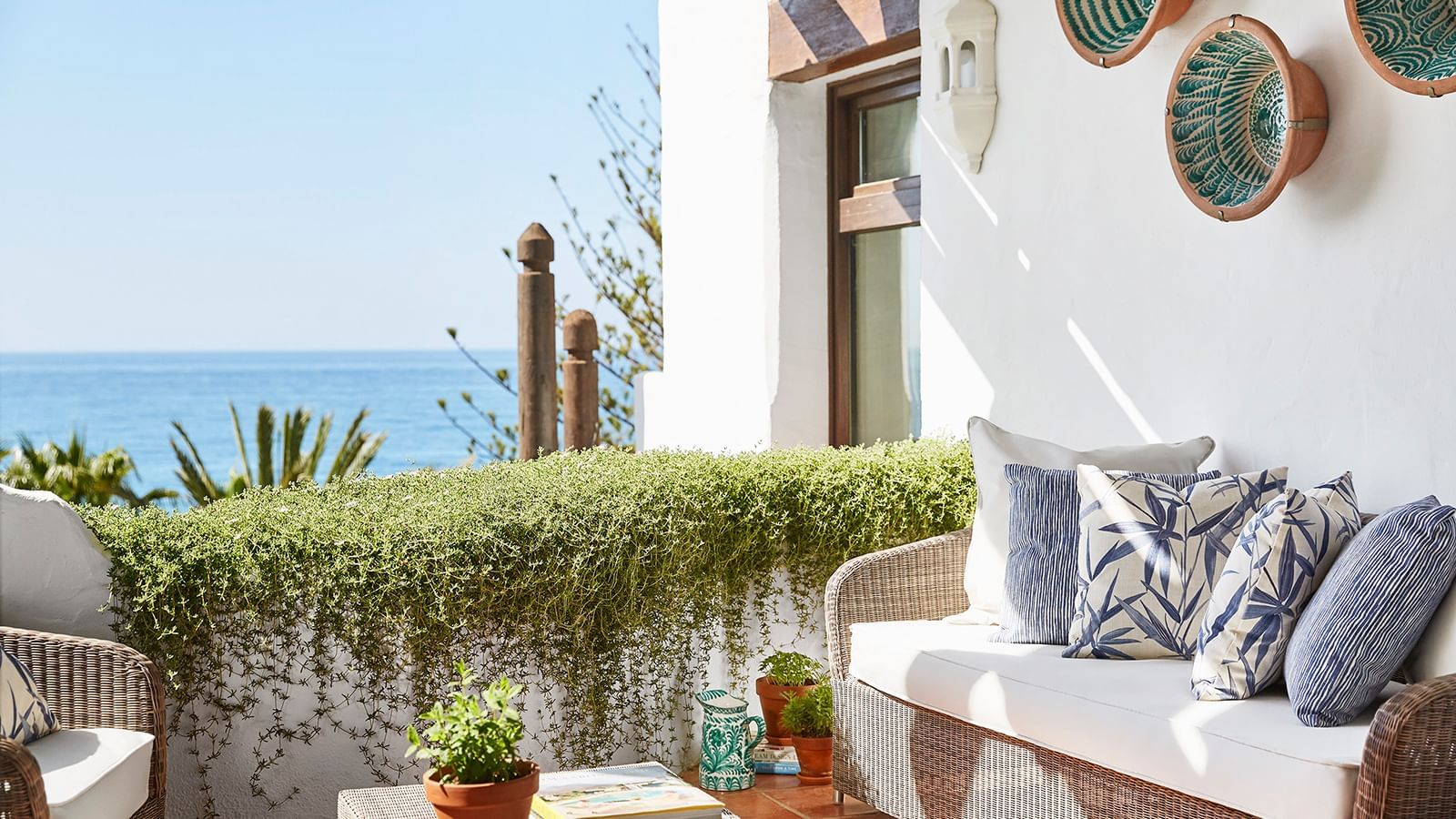 Ocean-view terrace with a wicker sofa placed by a white wall and green vine railing at Marbella Club