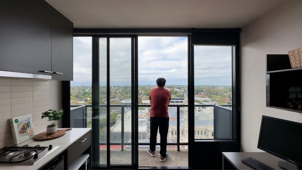 A resident stands at a balcony, contemplating space needs for living as a student.