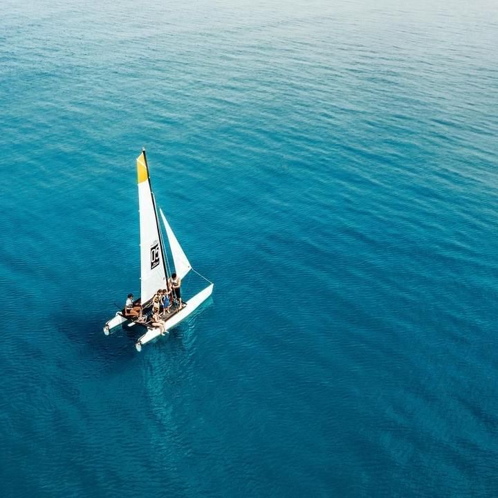 Veliero a vela con vela bianca e gialla e persone a bordo che naviga in acque blu.