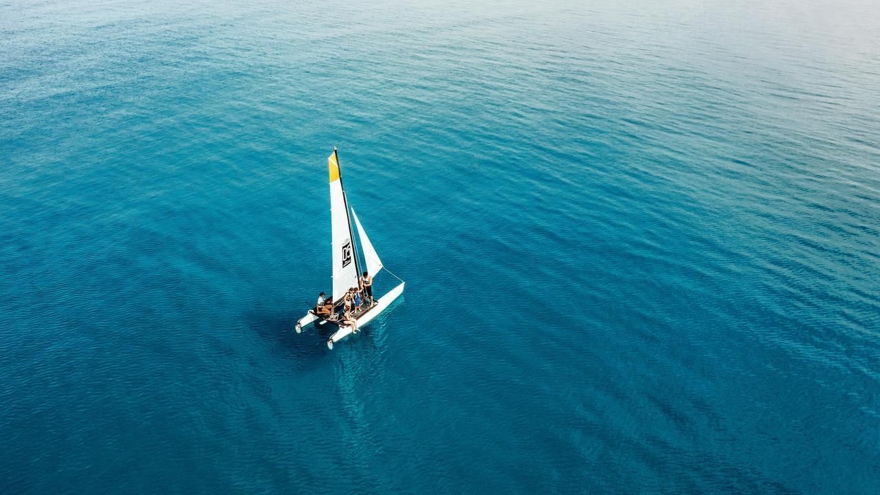 Luftaufnahme eines Katamarans mit Segel im blauen Meer, Passagiere an Bord.