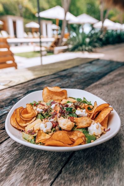 Fresh salad with crispy croutons and chips on an outdoor wooden table in a restaurant at El Mangroove Hotel