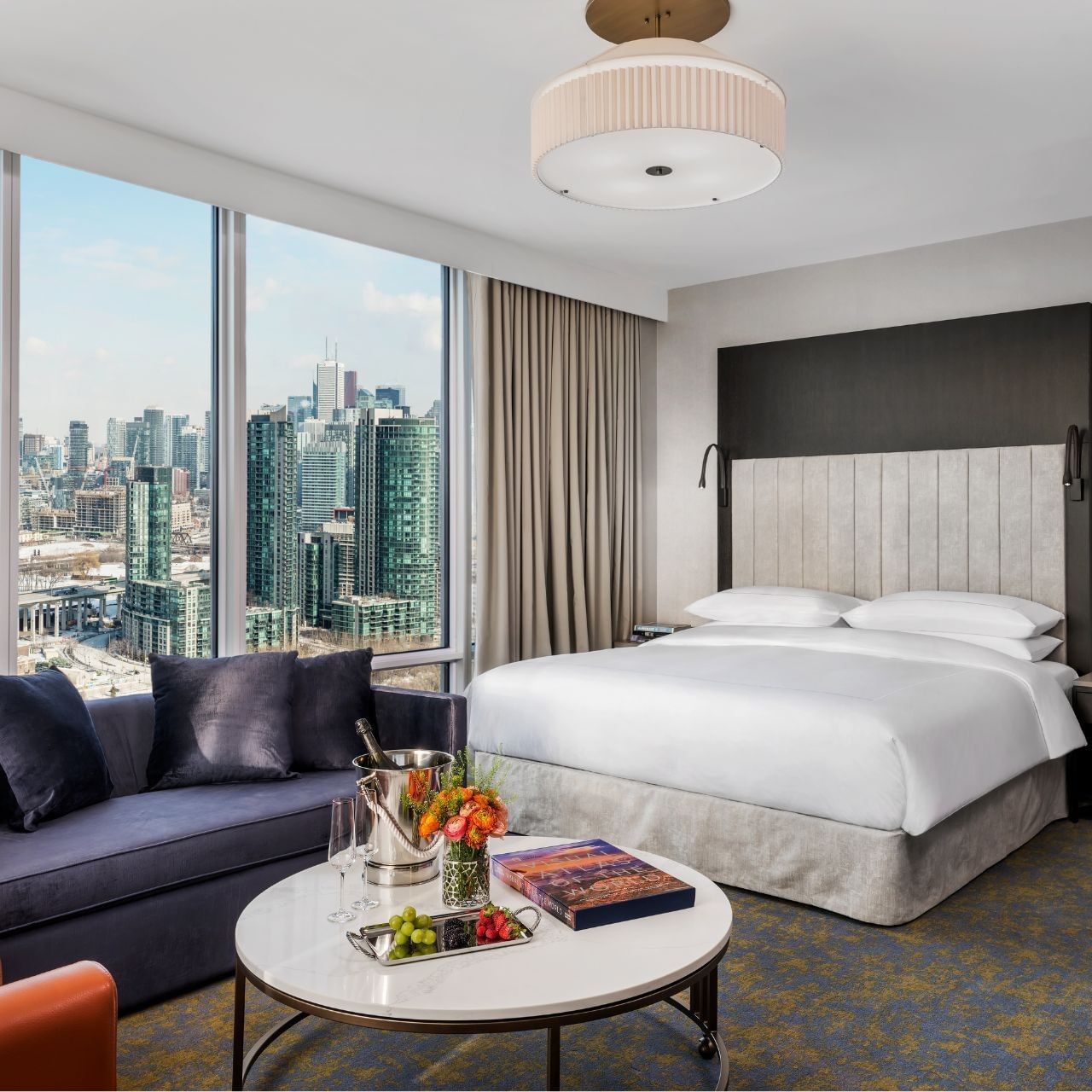 Family Two Bedroom Corner with a white bed and sofa by floor-to-ceiling city-view windows at Hotel X Toronto
