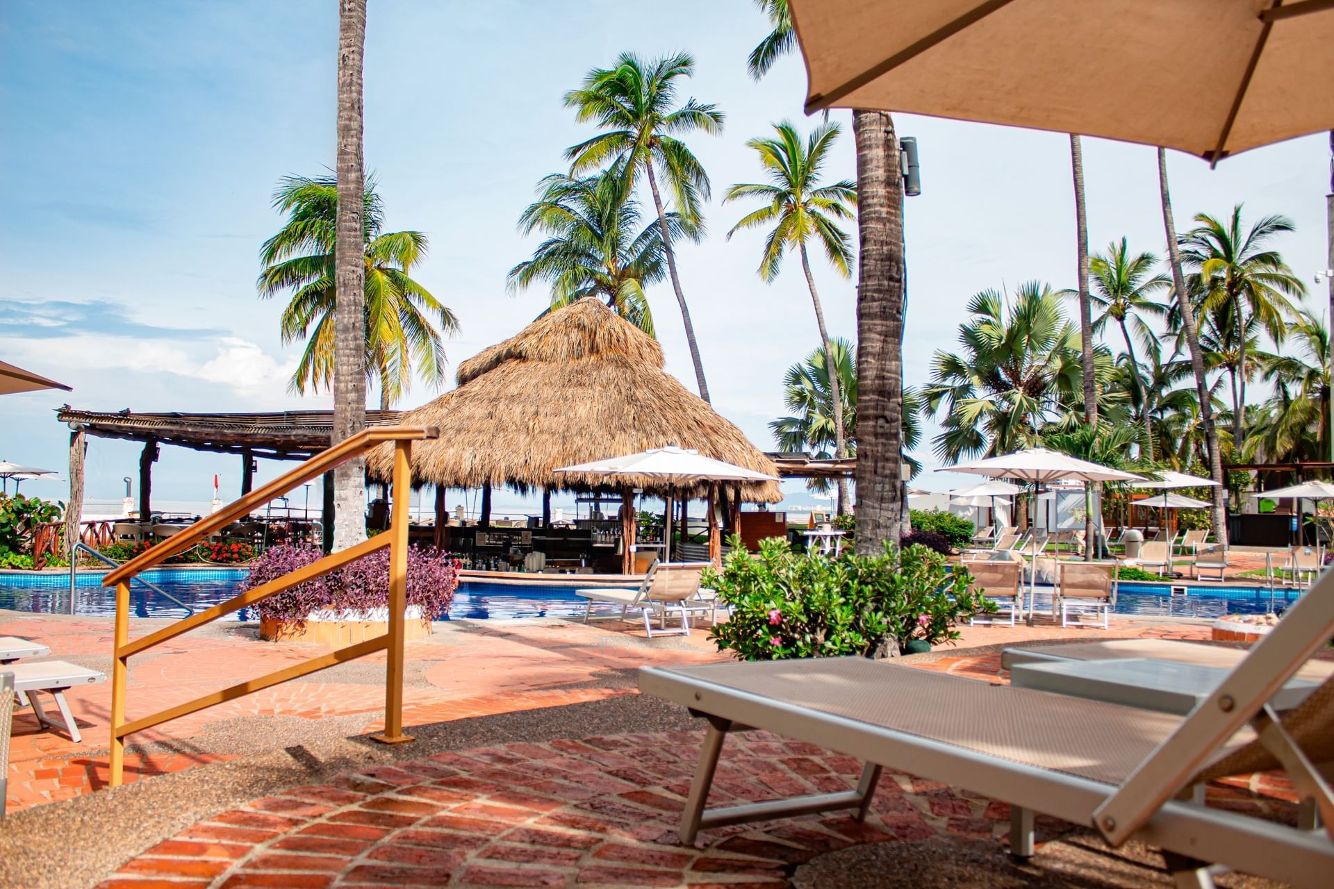Lounge chairs by the pool surrounded by palm trees at Plaza Pelicanos Grand Beach Resort