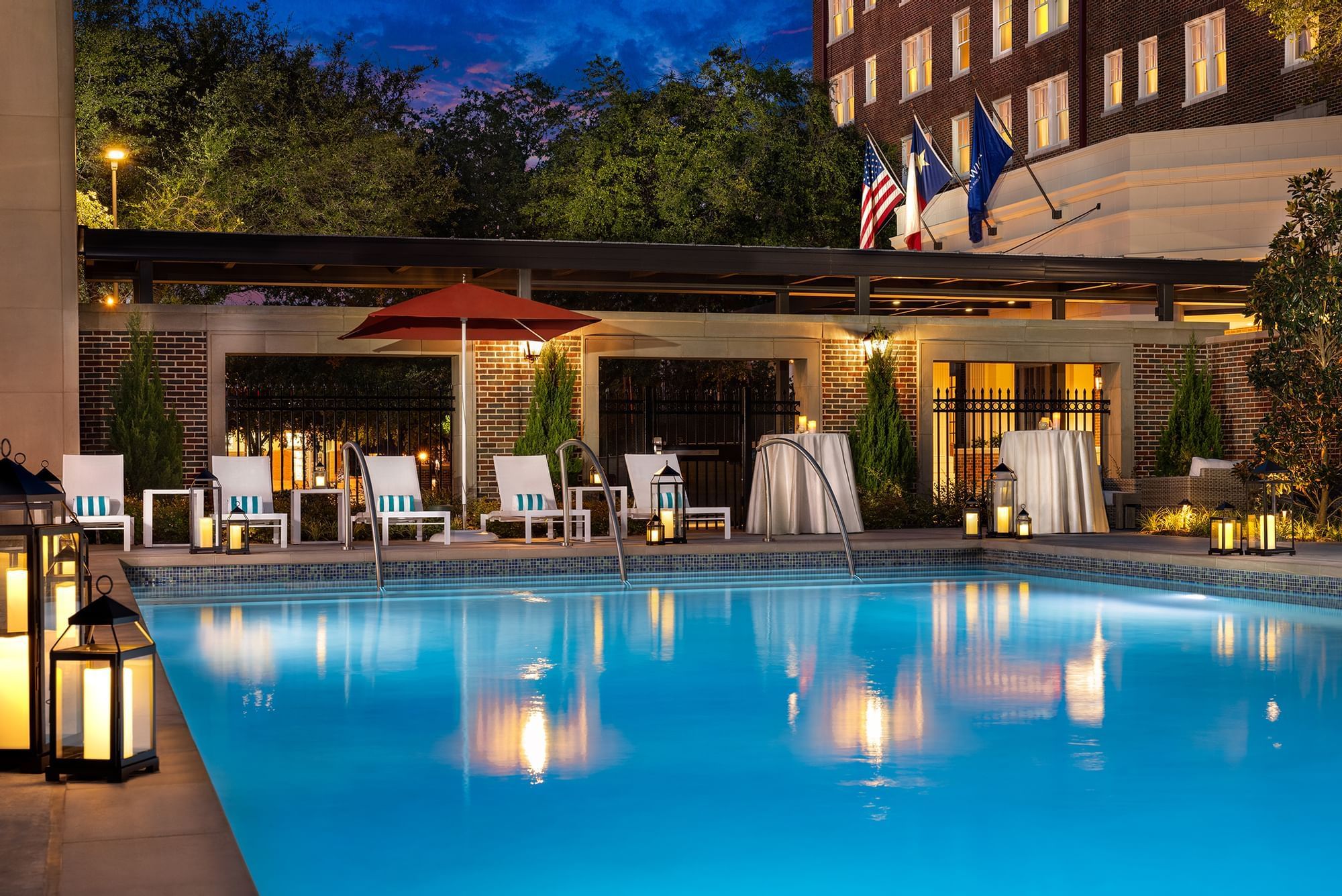 A serene outdoor pool scene at dusk with lounge chairs, umbrellas, and warm lighting.