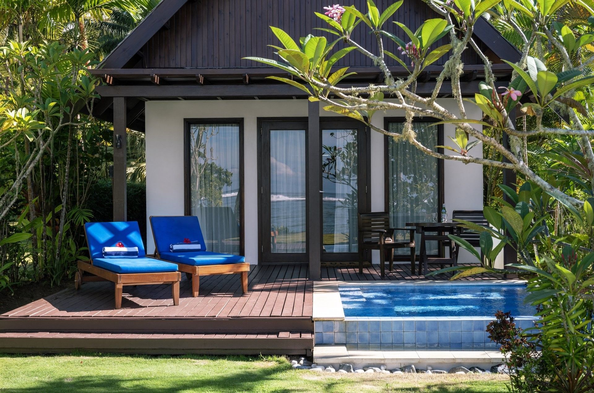 Blue lounge chairs by a private pool on a wooden deck under a leafy tree at Tambua Sands Beach Resort