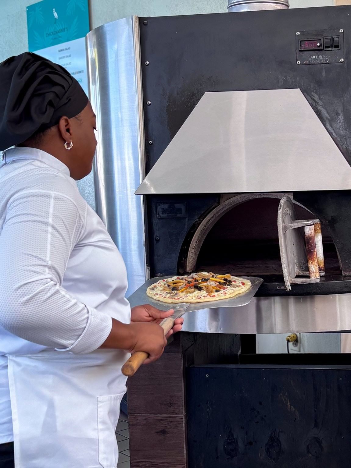 Chef placing a fresh pizza into a large stone oven in Chickcharnie's Pizzeria & Grille at Warwick Paradise Island Bahamas