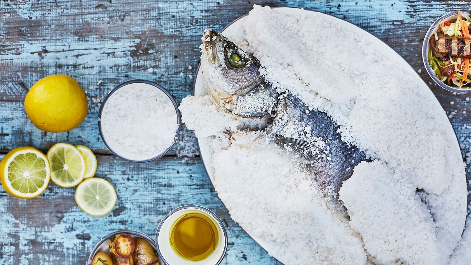 Whole fish completely encased in rock salt, presented on a plate resting on a blue wooden table at the Marbella Club