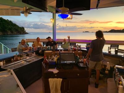 Patrons at a covered open-air beach bar with drinks overlooking a sunset ocean view at the Emerald Beach Resort