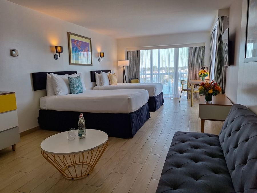 Harbour Premium Balcony with two beds by a sofa under wall lamps near a long desk at Warwick Paradise Island Bahamas