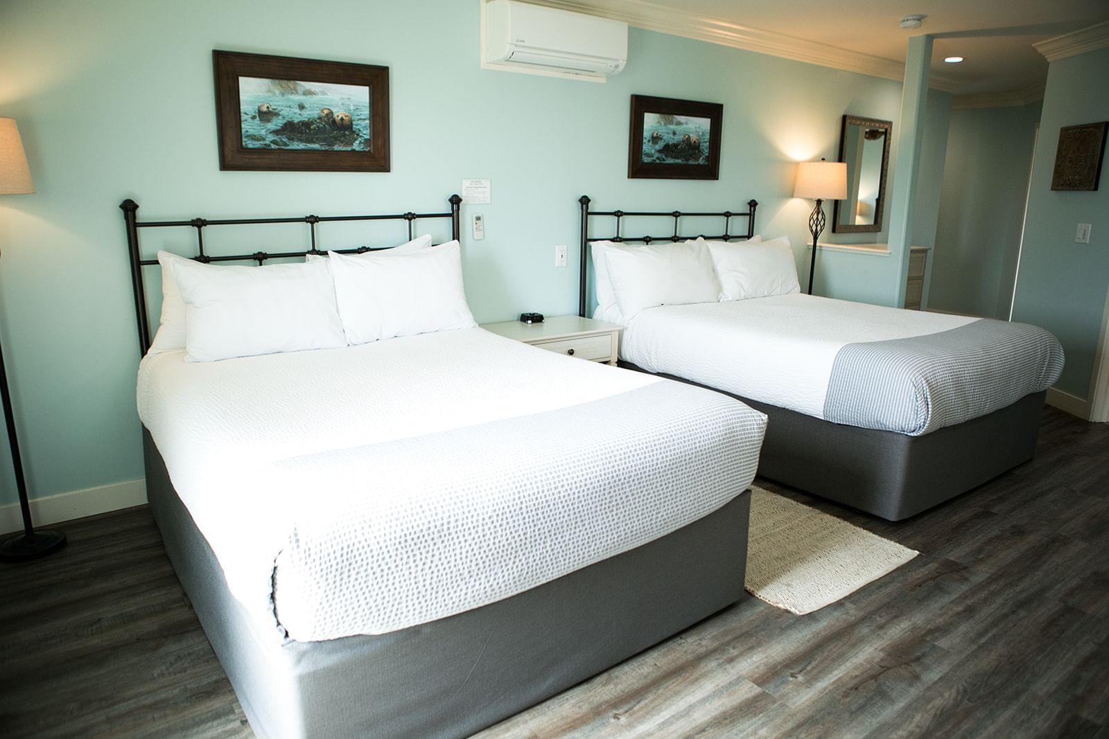 A hotel room with two beds, light blue walls, and dark wood flooring.