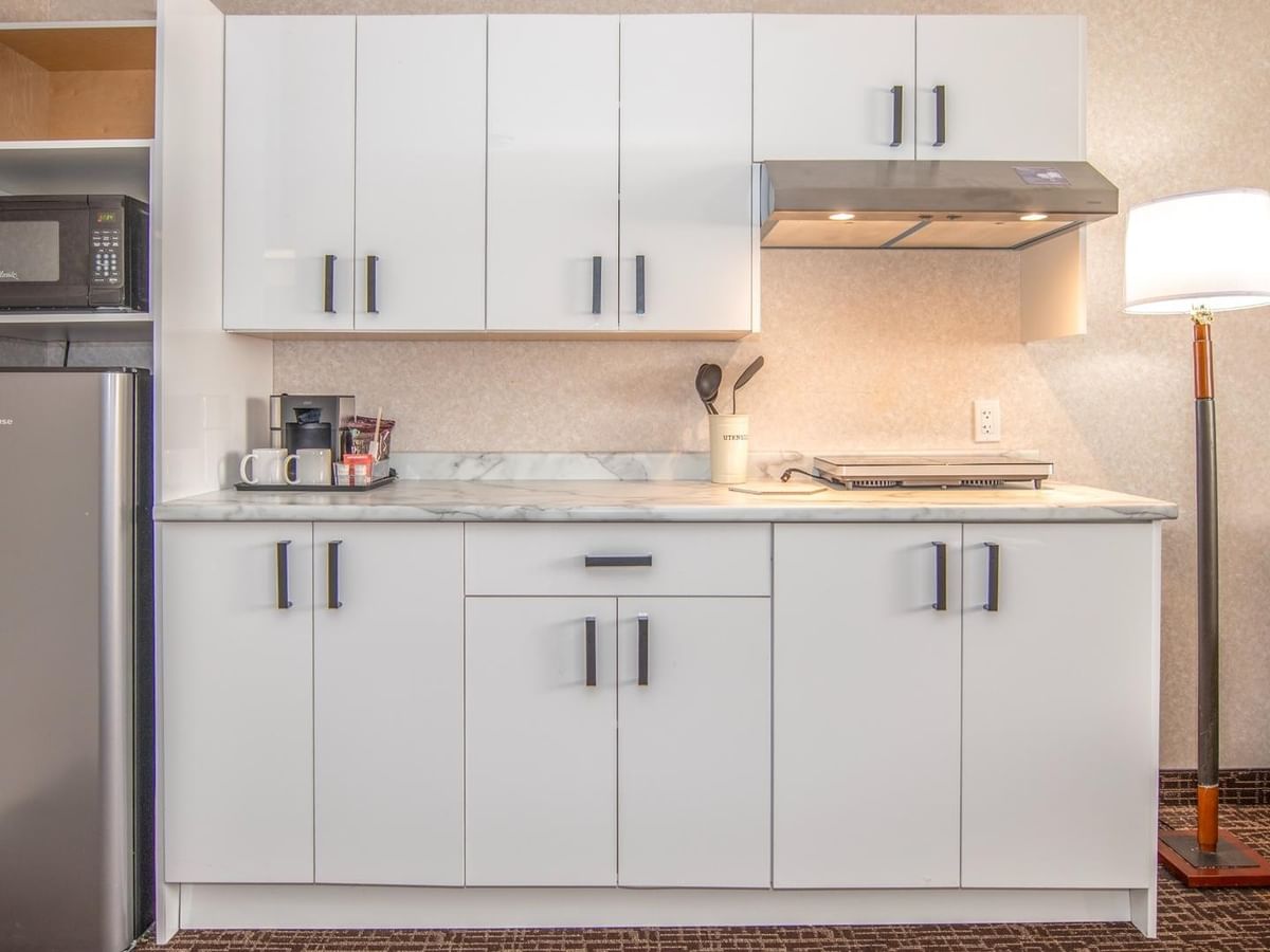 Kitchenette with white cabinets, microwave, refrigerator, countertop, and a floor lamp.