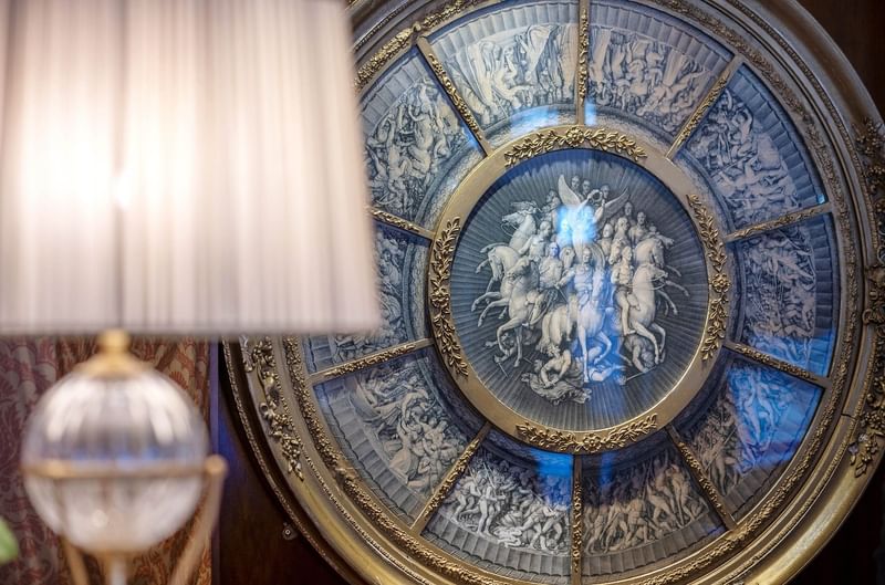 Ornate circular mural featuring classical figures and horses, framed in gold by a lamp at Warwick Grand Place Brussels