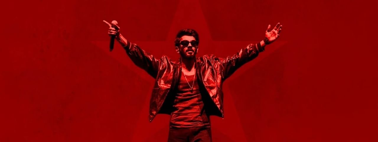 Anirudh Ravichander performing with microphone on stage with arms raised and red background for Anirudh XV Tour 2026.