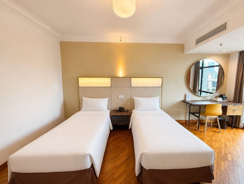 Wooden desk and a large round mirror by the plush beds in the Standard Twin Room with hardwood floors at YWCA Fort Canning