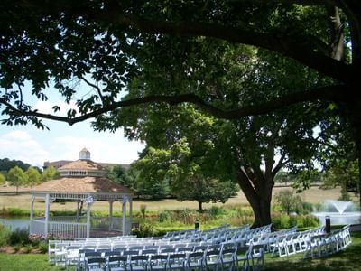 Outdoor wedding ceremony setup with white chairs arranged on lawn near gazebo and pond at Aramark Chauncey Conference Center