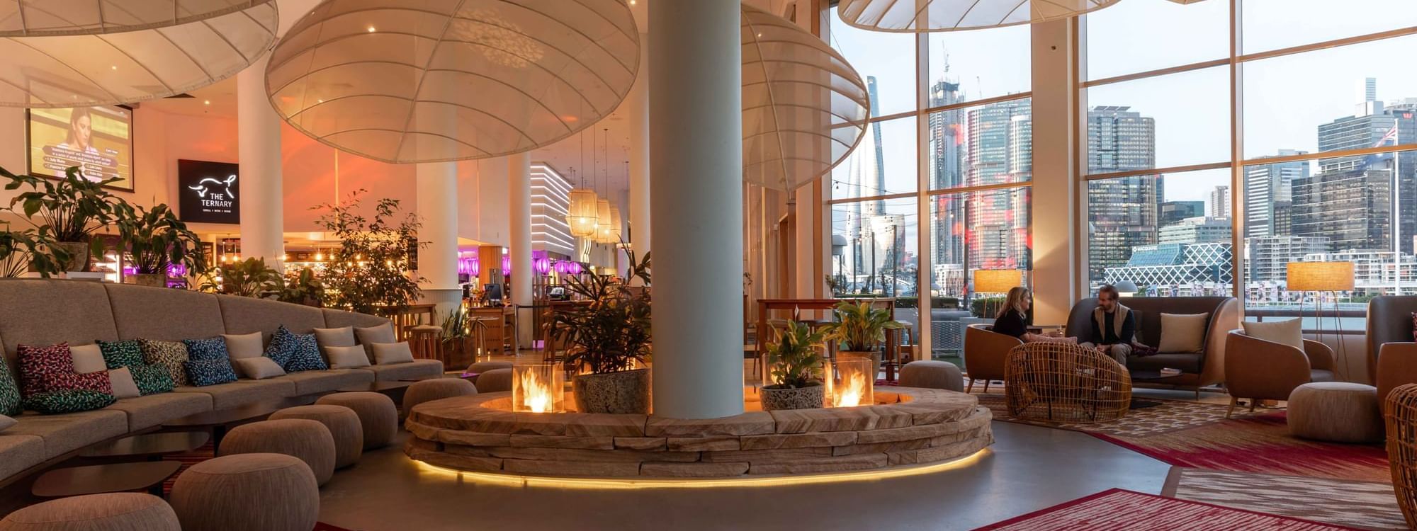The Chemney Lounge featuring a glowing fire pit, plush seating, and sweeping city views at Novotel Sydney on Darling Harbour