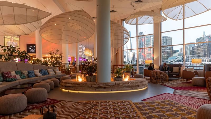 The Chemney Lounge featuring a glowing fire pit, plush seating, and sweeping city views at Novotel Sydney on Darling Harbour