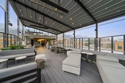 Terraza moderna con sofás y mesas, luces cálidas y vista panorámica de ciudad y montañas.
