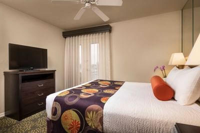 Guest room with white bedding, decorative bed runner, ceiling fan, and TV at London Bridge Resort