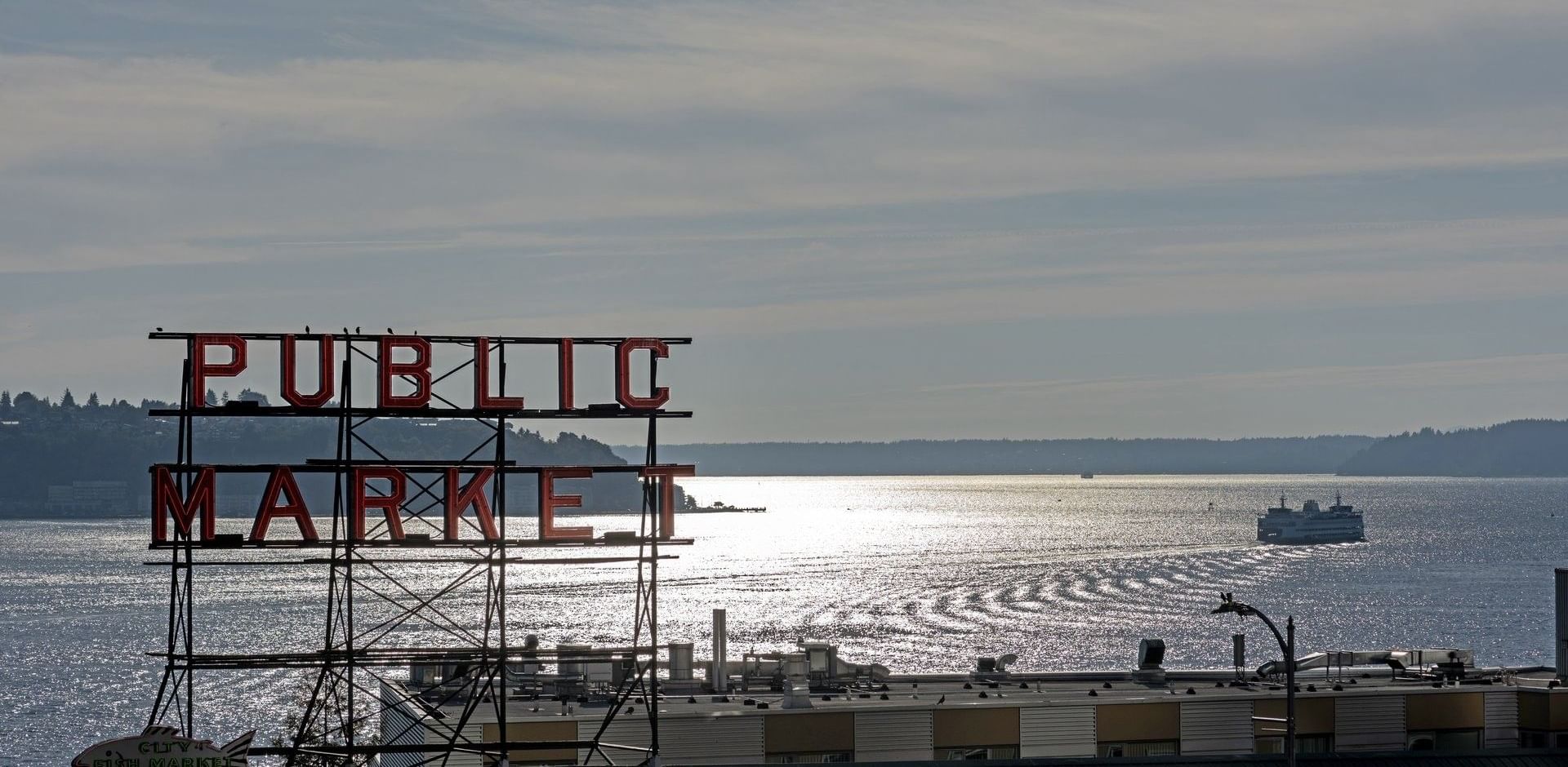 View of Public Market sign over water with a ferry in the distance near Warwick Seattle