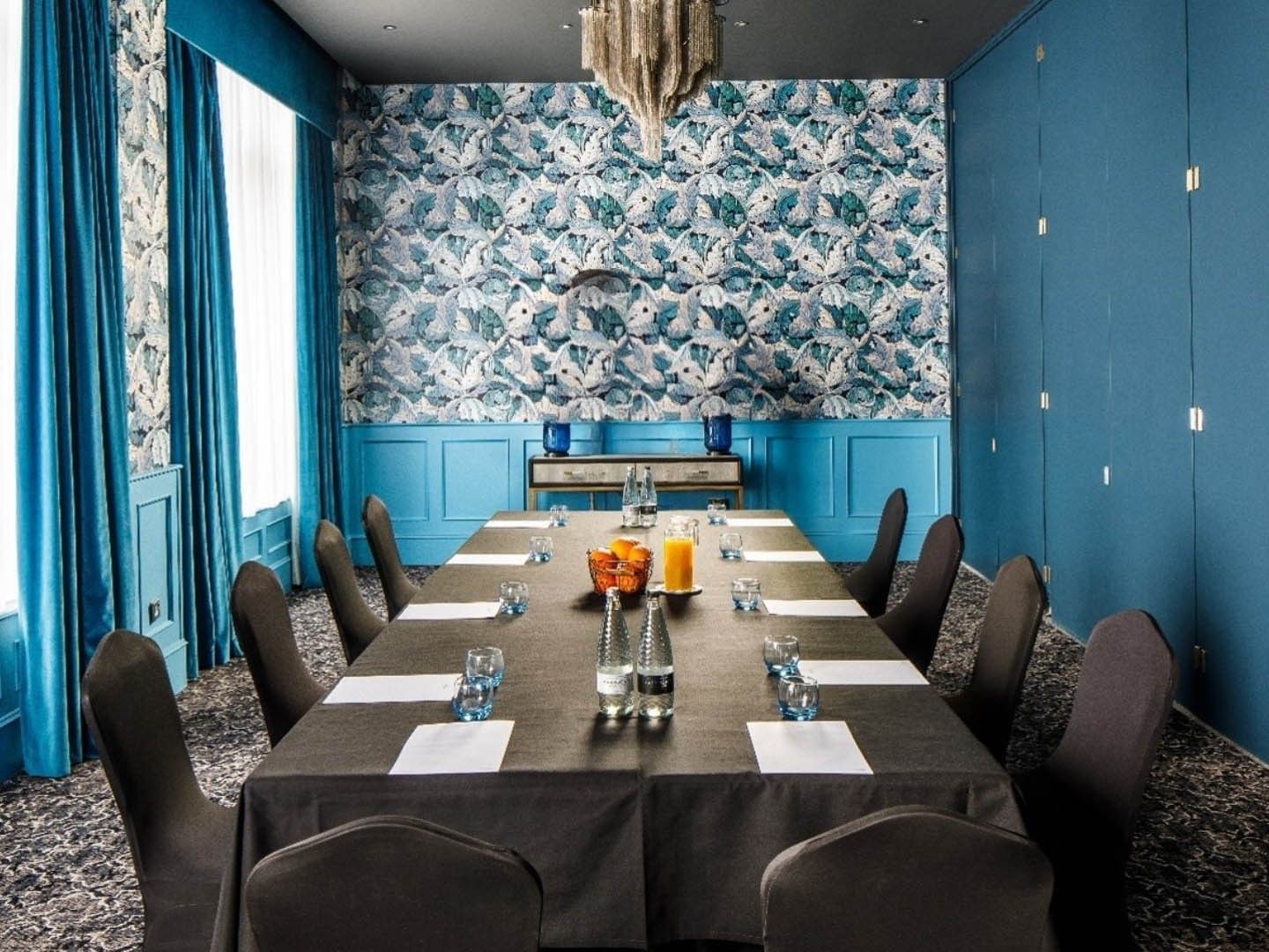 Blue and teal meeting room with long table, chairs, and patterned wallpaper, showcasing a modern and sophisticated design.