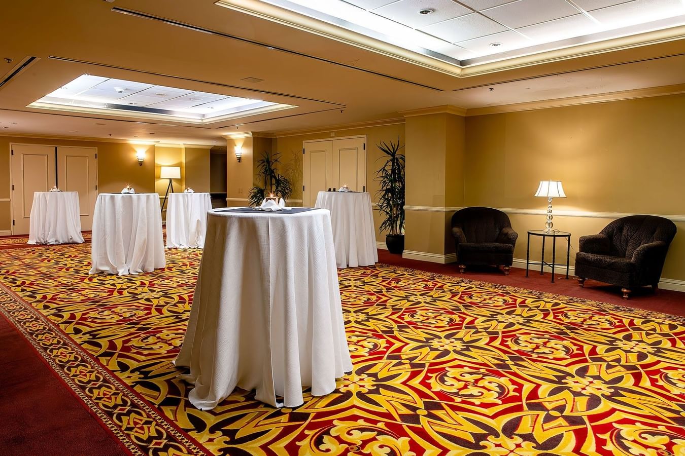 Tall cocktail tables with white cloths on a patterned carpet by plush armchairs in Capitol Ballroom at Warwick Denver