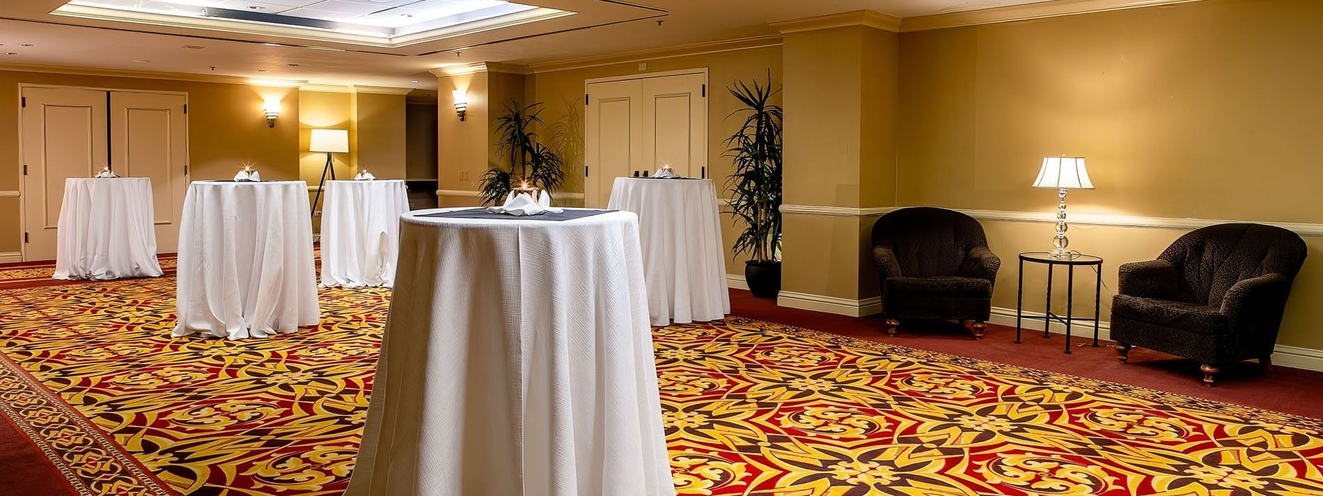 Tall cocktail tables with white cloths on a patterned carpet by plush armchairs in Capitol Ballroom at Warwick Denver
