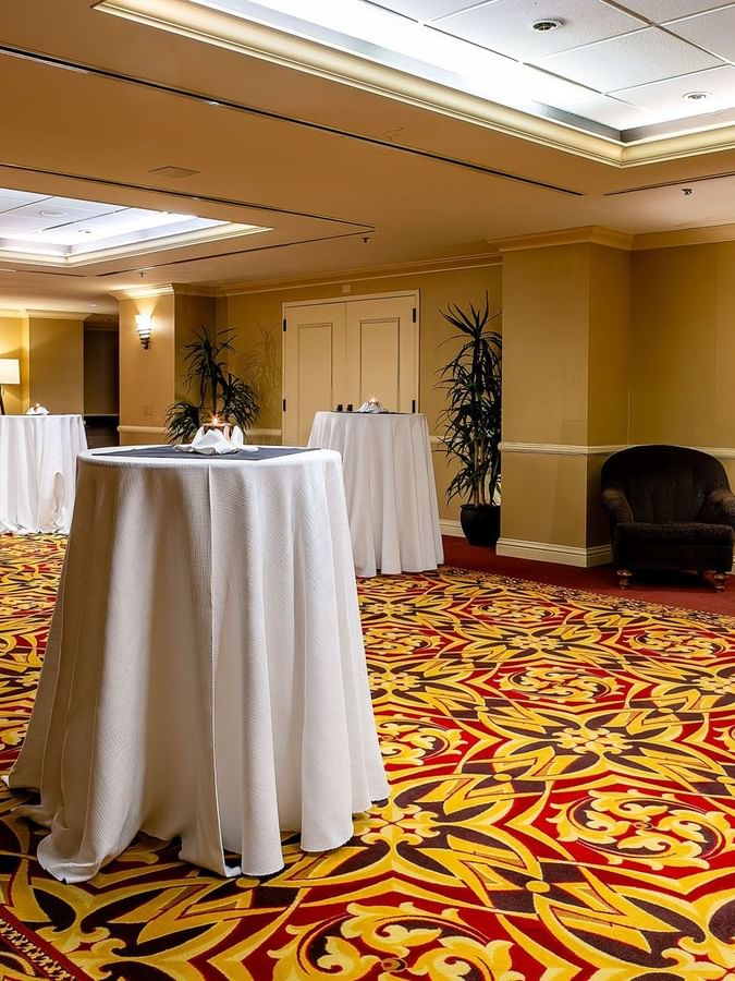 Tall cocktail tables with white cloths on a patterned carpet by plush armchairs in Capitol Ballroom at Warwick Denver