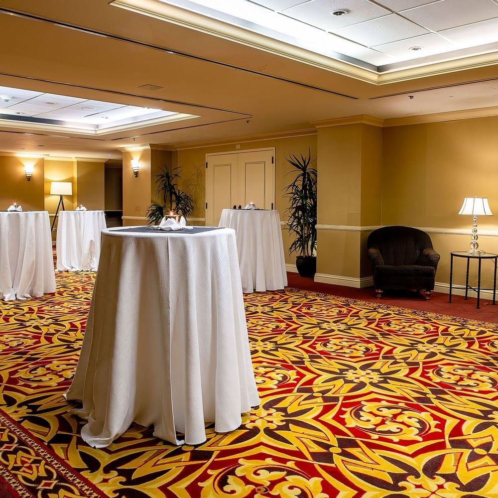Tall cocktail tables with white cloths on a patterned carpet by plush armchairs in Capitol Ballroom at Warwick Denver