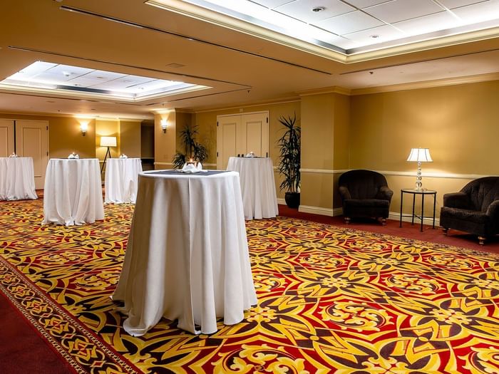 Tall cocktail tables with white cloths on a patterned carpet by plush armchairs in Capitol Ballroom at Warwick Denver