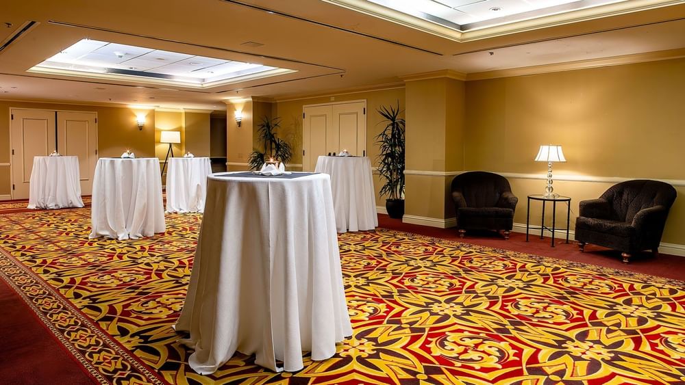 Tall cocktail tables with white cloths on a patterned carpet by plush armchairs in Capitol Ballroom at Warwick Denver