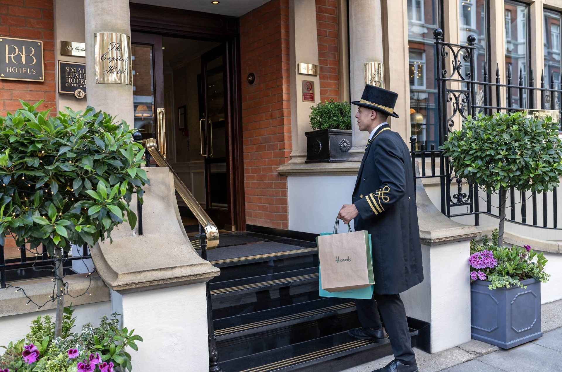 Uniformed doorman carrying Harrods shopping bags, walking up stone steps at The Capital Hotel, Apartments and Townhouse