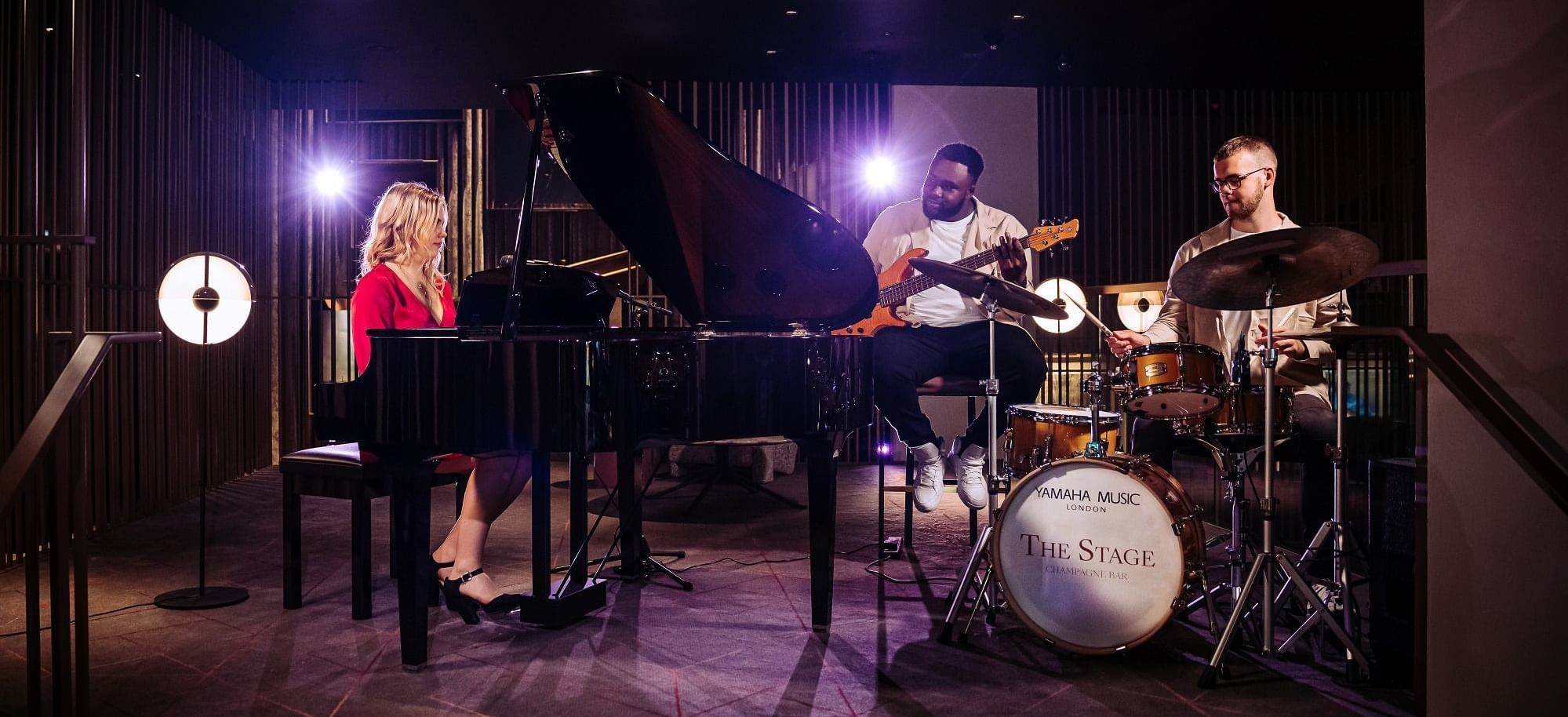 Lively band performs on The Stage with grand piano, guitar, and drums at The Londoner