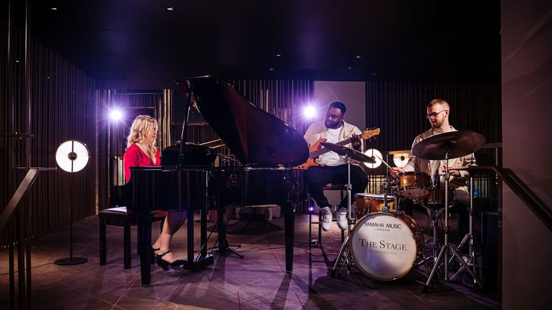 Three people performing a live band show on a stage at The Londoner Hotel