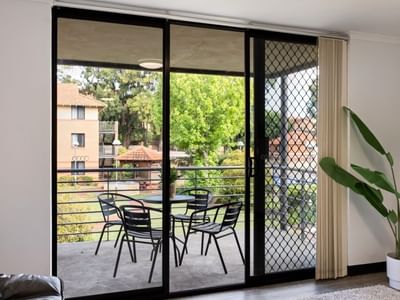 Glass balcony with table and chairs, and a potted plant inside, at UniLodge at Curtin University - Erica Underwood House.