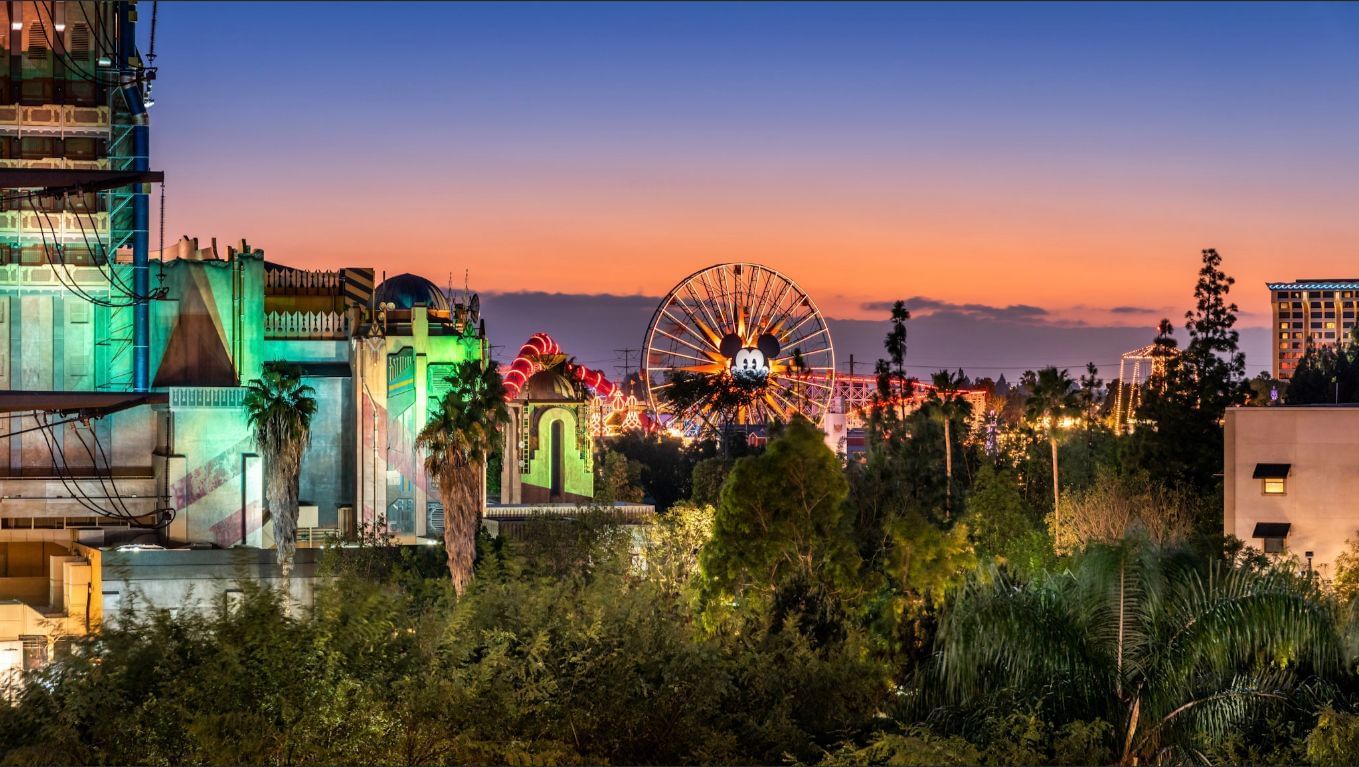 A wide exterior view of a building with trees and a Ferris wheel in the background at dusk.