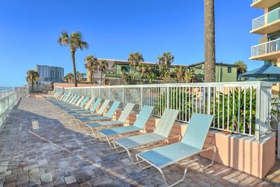 Row of lounge chairs at the beachfront patio of the Daytona Bahama House Hotel with railing and palm trees