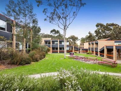 Exterior of La Trobe University – Menzies College with buildings, lawn, and benches under blue sky.