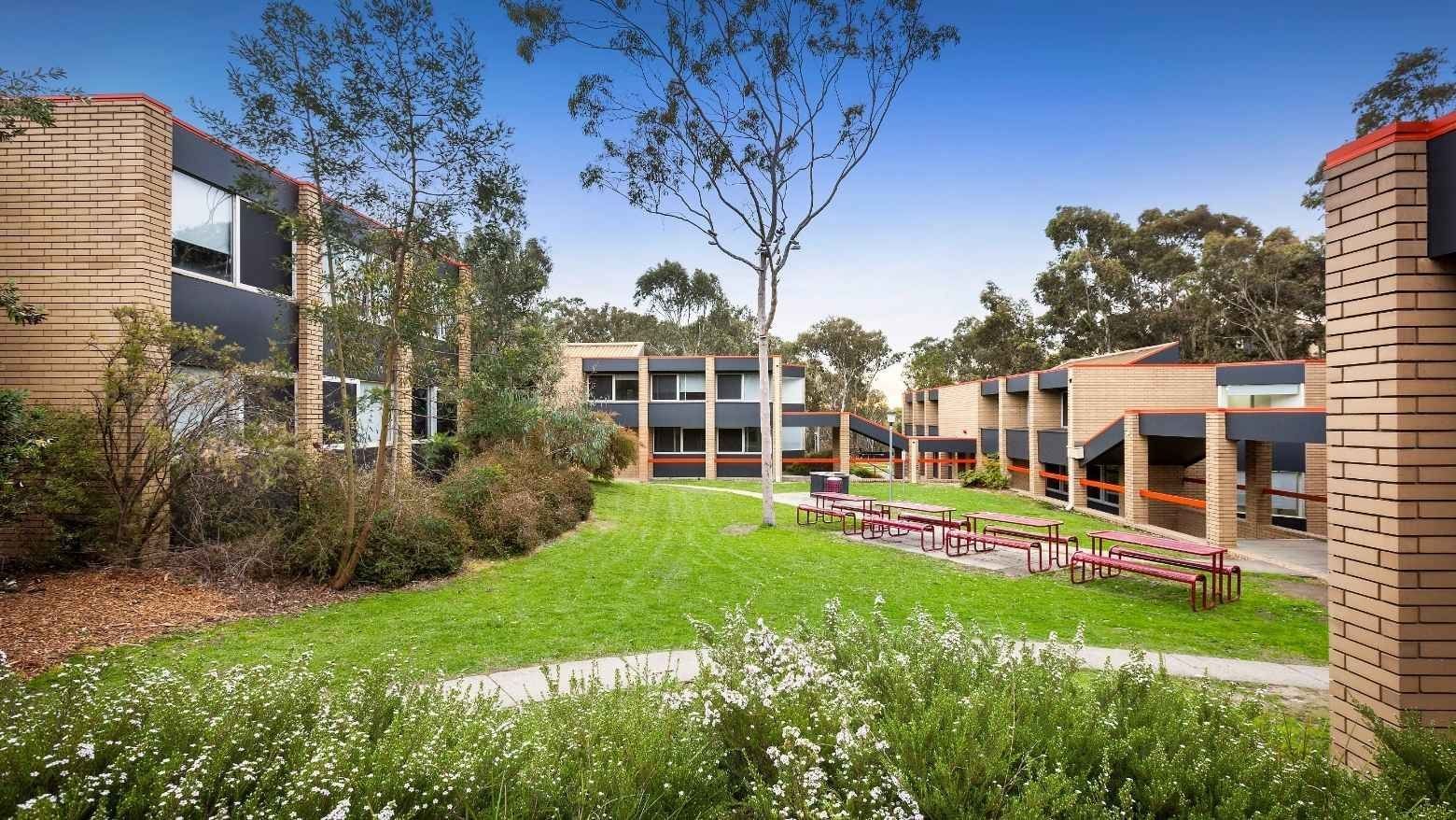 Exterior of La Trobe University – Menzies College with buildings, lawn, and benches under blue sky.
