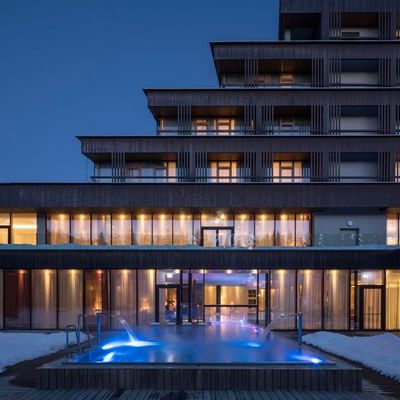 Modernes Gebäude mit beleuchteten Fenstern und beleuchtetem Außenpool bei Nacht.