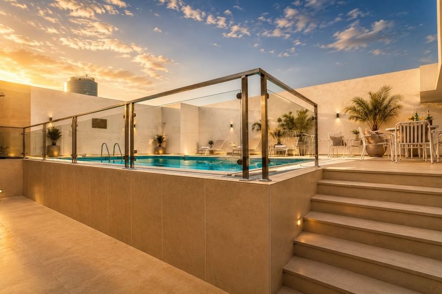 Rooftop swimming pool behind glass railings near sun loungers and dining sets under sunset sky at Naviti by Warwick Jeddah