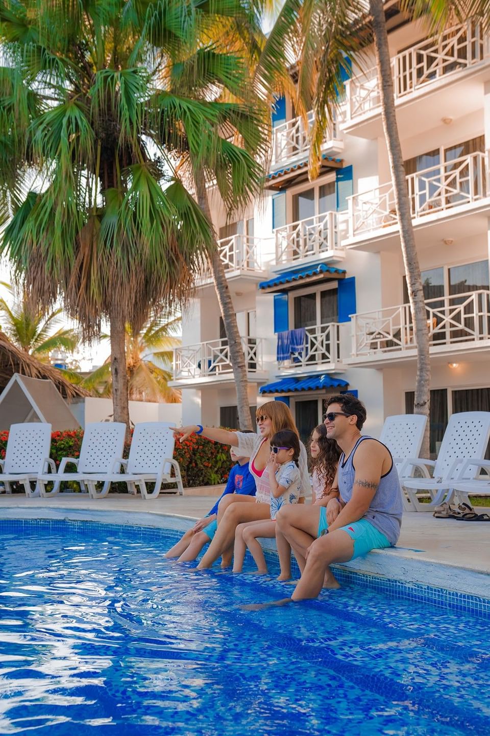 Family of four sitting poolside with palm trees and white balconies at Playa Blanca Beach Resort