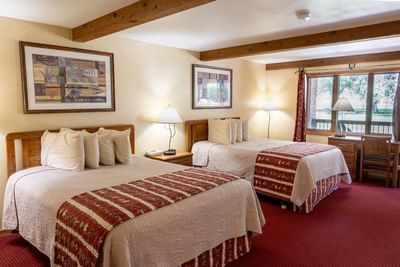 Nightstand by the cozy beds in Aspen Cabins with warm lighting and carpeted floors at The Ranch at UCross