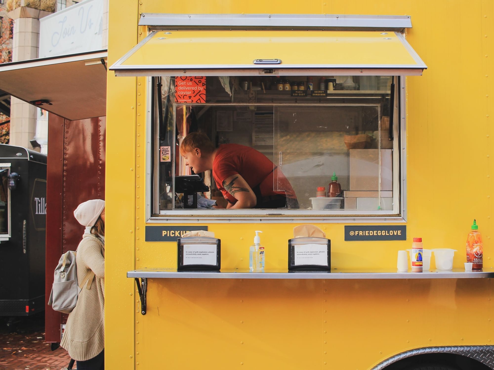 A woman ordering food from a man on a yellow food truck.