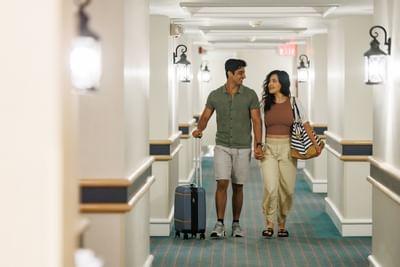 Couple with luggage walking in a hallway under lamps at Rodd Brudenell River Resort, a premier place to stay in PEI
