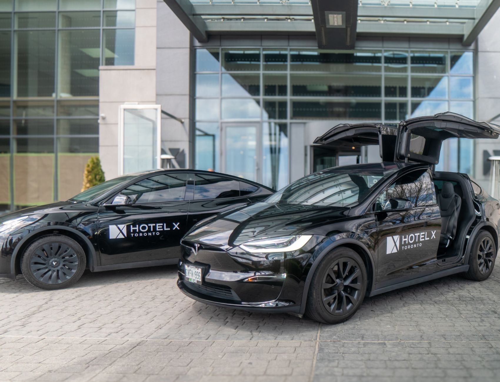 Black Tesla vehicles parked by the entrance at Hotel X Toronto, with one featuring open falcon-wing doors under a canopy
