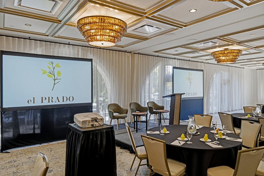 meeting room set up at el PRADO with projected screens towards the front of the room, alongside a speaker podium