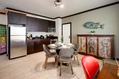 Apartment dining area and kitchen with a glass table, dark wood cabinets, and a sideboard at Tradewinds Apartment Hotel