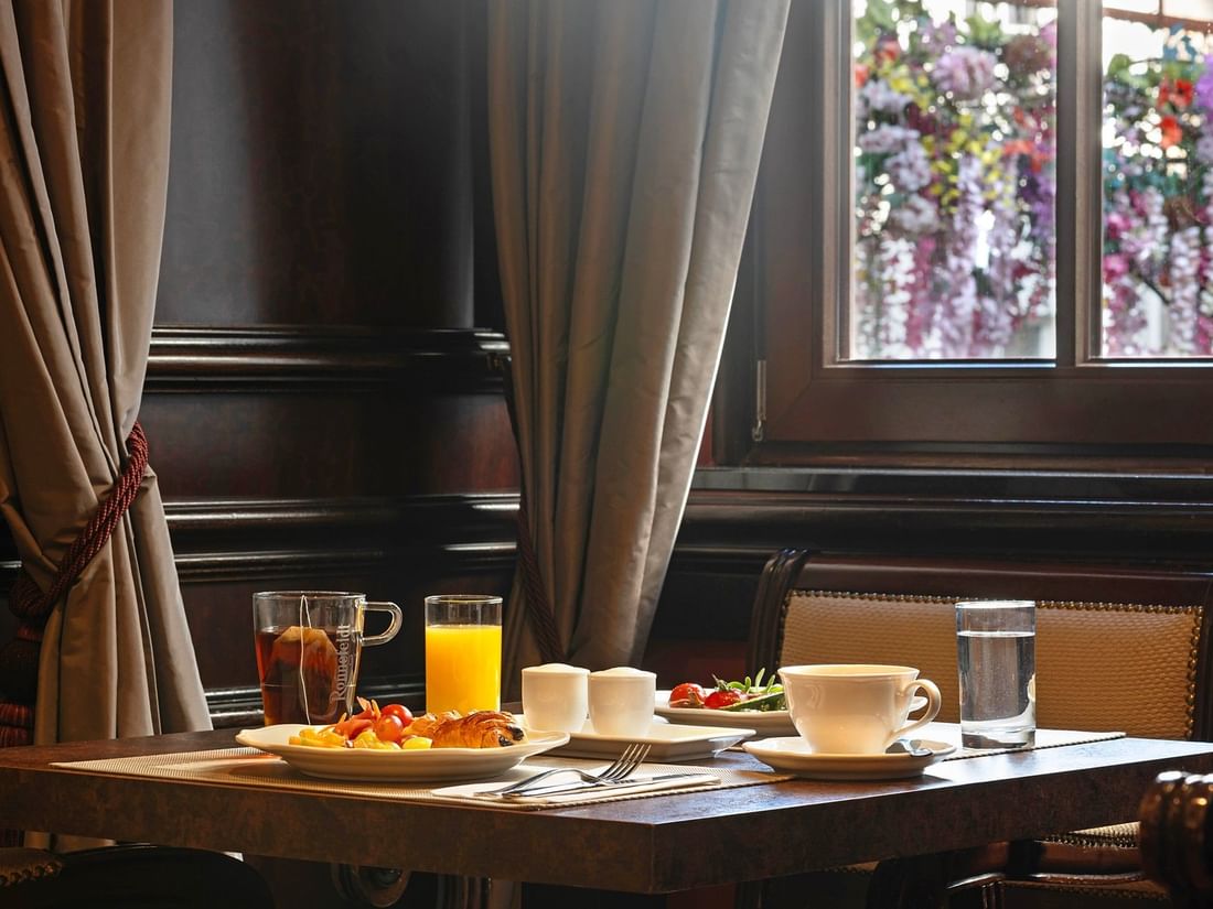 Breakfast table with a cup of tea placed by a plate of pastries near a window at Warwick Grand Place Brussels